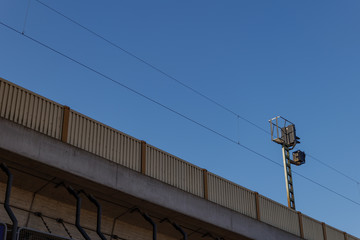 Low angle under concrete railway or railroad, noise concrete absorbing noise barriers modular, and electric post with cable over track against background of blue sky.