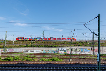 Outdoor sunny view of red train with  graffiti from DB, Deutsche Bahn German train company, run on railroad and foreground of railways in Cologne, Germany. 