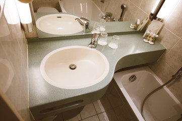 Interior of modern three star hotel bathroom with sink, chrome water tap , two glasses and defocused shampoo in the corner