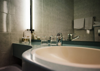 Interior of modern three star hotel with sink, chrome water tap, two glasses and defocused shampoo in the corner