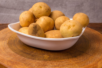 Fresh and raw potatoes stacked in a round dish on wooden table. Rustic style..