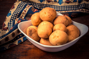 Fresh and raw potatoes stacked in a round dish on wooden table. Rustic style..
