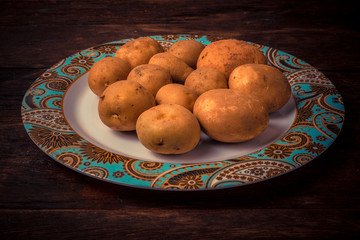 Fresh and raw potatoes stacked in a round dish on wooden table. Rustic style..