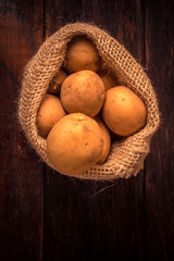 Fresh and raw potatoes in a rustic sack on wooden table.
