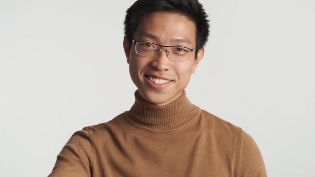 Young attractive stylish asian man in eyeglasses happily straightens hair on camera isolated. Pickup master