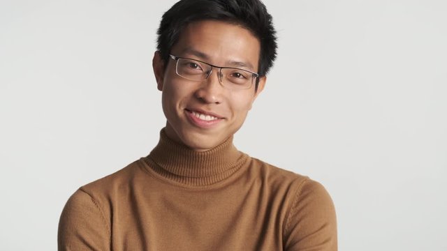 Smart smiling stylish asian man in eyeglasses happily looking in camera isolated