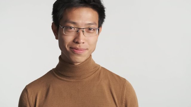 Young attractive stylish asian man in eyeglasses joyfully flirting on camera isolated