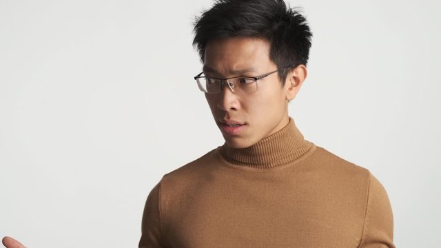 Young stylish perplexed asian man in eyeglasses over white background. What is going on expression