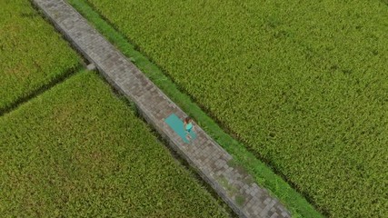 Aerial Slowmotion shot of a young woman practicing yoga on a beautiful rice field