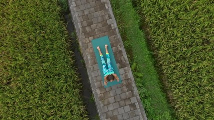 Aerial Slowmotion shot of a young woman practicing yoga on a beautiful rice field