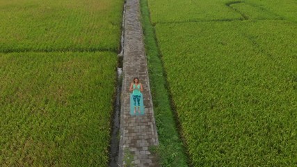 Aerial Slowmotion shot of a young woman practicing yoga on a beautiful rice field