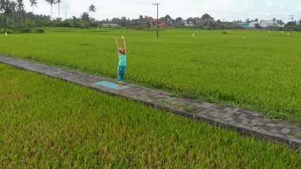 Aerial Slowmotion shot of a young woman practicing yoga on a beautiful rice field