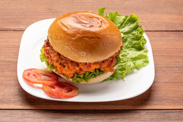 Homemade cheeseburgers with lettuce and tomato in a white plate on wooden background