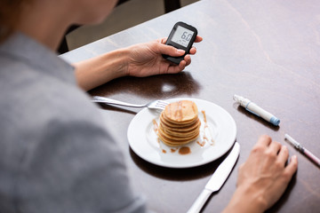 selective focus of woman with diabetes holding glucose monitor near pancakes