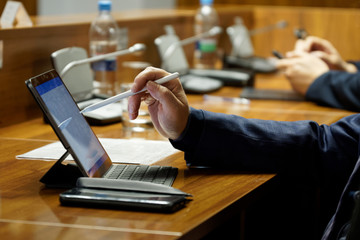 Men in suits during a business meeting. One of them - an official, businessman or deputy uses the touch screen of a tablet computer. Close-up - obrazy, fototapety, plakaty