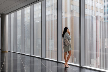 Attractive young woman of mixed race talking on cell phone while looking out the window of bright modern office lobby, 