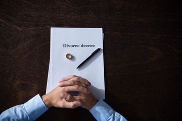 partial view of man sitting at table with clenched hands with divorce documents