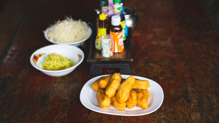 Asian congee with minced pork, sliced ginger, vegetable and mini deep-fried dough sticks in glass bowl on wooden table. a delicious traditional Asian food style
