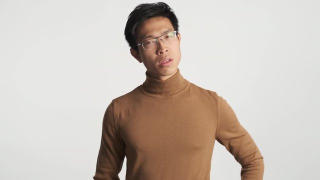Young serious asian man in eyeglasses disappointedly showing whatever gesture and leaving shot isolated. No matter expression