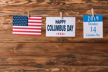 card with happy Columbus day inscription near American national flag and calendar paper sheet with 14 October date on wooden surface