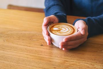 Closeup image of a woman holding a cup of hot coffee on wooden table