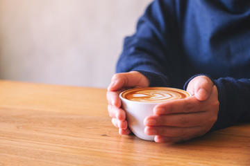 Closeup image of a woman holding a cup of hot coffee on wooden table