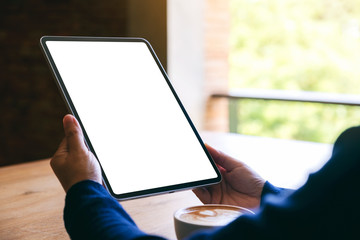 Mockup image of a woman holding black tablet pc with blank white screen with coffee cup on wooden table