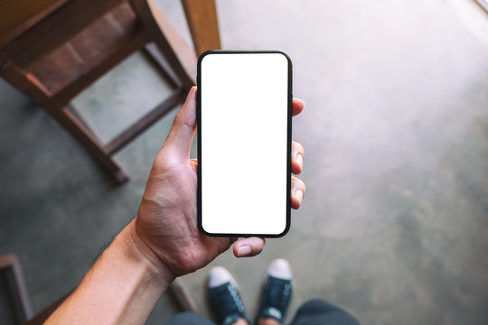 Top view mockup image of a man standing and holding black mobile phone with blank white screen