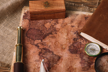 wooden box, telescope, compass and aged world map on hessian