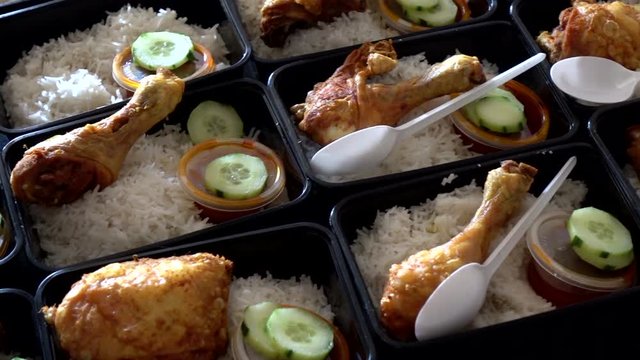 A row of Nasi Lemak with Chicken Roasted in lunch boxes container while hands put a plastic spoon with it.