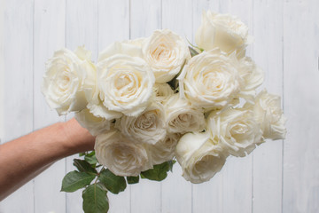 Hand holding white roses bouquet on white wooden background. Love concept. Top view.