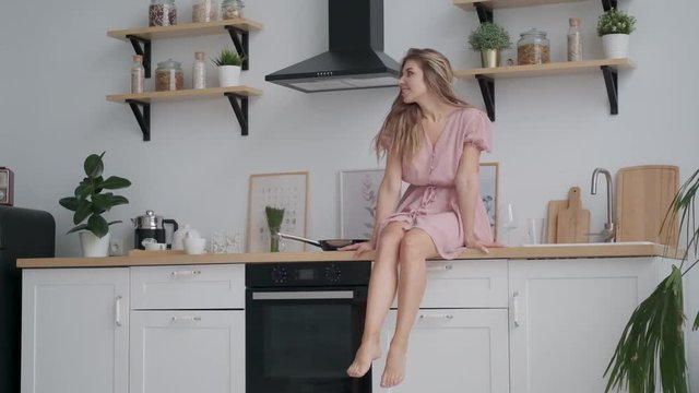 happy girl sitting on the kitchen table and carefree dangles legs