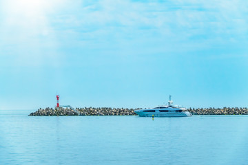 A large white yacht leaves the port. The yacht is sailing next to the lighthouse.