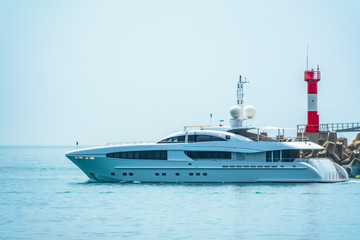 A large white yacht leaves the port. The yacht is sailing next to the lighthouse.