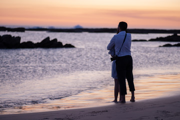 Young couple standing on beach and viewing sunset over the horizon