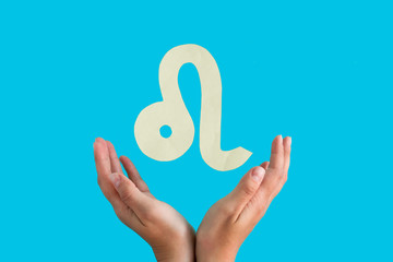 Leo astrological sign hanging over female hands on blue background, horoscope forecast concept