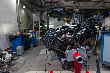 Replacement used engine mounted on a crane for installation on a car after a breakdown and repair in a car repair workshop as a guarantee for the dealership. Auto service industry.