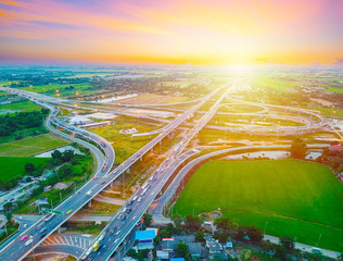 Aerial view of a massive highway intersection, Highway to city transport traffic road with vehicle movement at sunset, Rural asphalt road scenery with sunshine. Transportation and industrial concept.