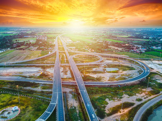 Aerial view of a massive highway intersection, Highway to city transport traffic road with vehicle movement at sunset, Rural asphalt road scenery with sunshine. Transportation and industrial concept.