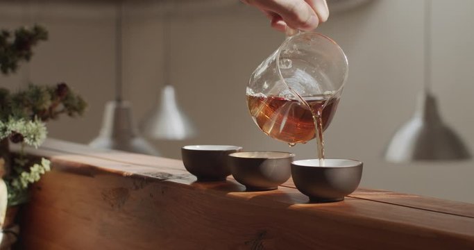 Faceless master pouring boiling water into cups with sun reflection natural light slow motion. Beautiful tea ceremony in calm place close up wooden bamboo table. Tranquility zen meditation calmness