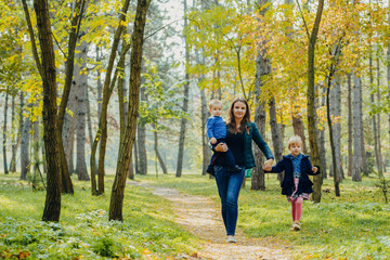 Fototapeta premium Mom with daughter and son are walking in the autumn park. Family for a walk in the forest