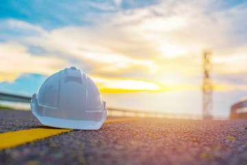 Close up of white safety helmet placed on the yellow solid line of road with sunset and blue sky...