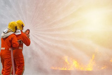 Two brave firefighter using extinguisher and water from hose for fire fighting, Firefighter spraying high pressure water to fire, Firefighter training with dangerous flames, Copy space-Image