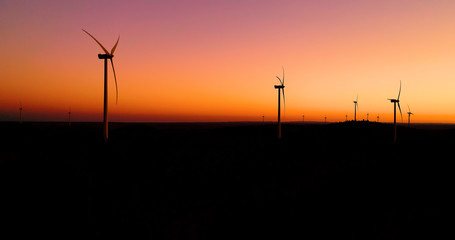 Wind turbines under the orange sunset. This is a wind farm which produce sustainable energy, perfect for the environment - aerial view with a drone - environmental & ecological concept