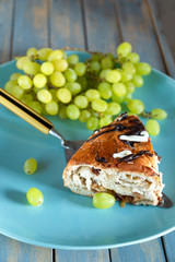Fresh piece of cake and grapes on a blue plate and wooden texture.