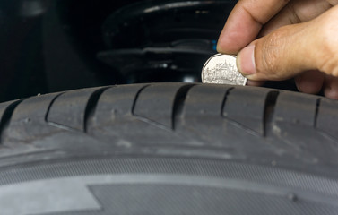 Man place a penny into tread grooves across the tire for checking tire tread depth and wear, Tire...