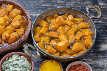 Baked yellow pumpkin with honey, anise, olive oil and spices on a plate on the wooden table. Vegetarian food. Closeup