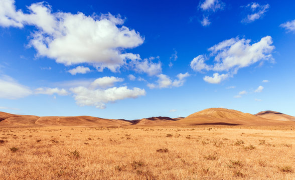Clouds on a blue sky over mountains with dried yellow grass