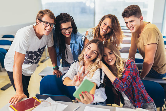 Joyful students doing group selfie on smartphone in classroom.