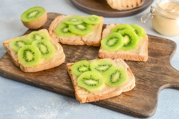 Tasty sandwiches with kiwi and peanut butter on wooden board
